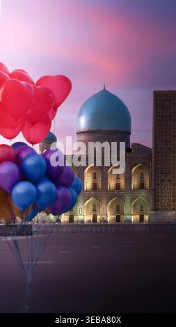 View of the blue dome and mosaic walls of Registan Square with colorful balloons in the foreground under a pink sunset sky in Samarkand, Samarqand Reg Stock Photo