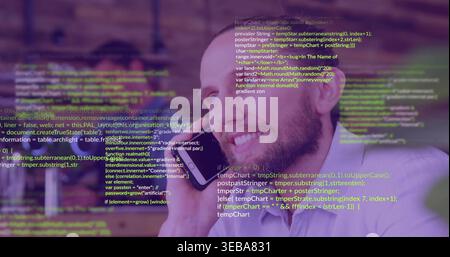 Smiling mid-adult man holding smartphone to ear, speaking at desk, in light shirt, code overlay Stock Photo