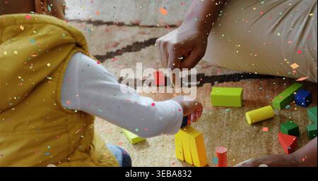 Stacking blocks child in yellow vest reaching toward yellow stack on rug, confetti overlay Stock Photo