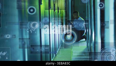 Kneeling tech wearing shirt checking tablet in data-center by open rack with holo HUD, copy space Stock Photo