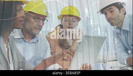 Discussing group of four professionals reviewing plans on laptop in site office, with hard hats Stock Photo