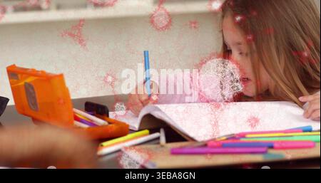 Writing girl wearing pink leaning over open notebook at desk holding blue pencil near orange case Stock Photo