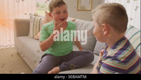 Talking two boys sitting on gray sofa in living room with patterned pillows, wearing green T-shirt Stock Photo