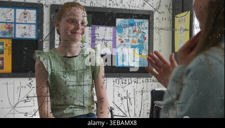 Seated girl in green ruffled blouse and denim watching instructor writing math on glass boards back Stock Photo