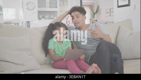 Sitting father grey-tee and daughter green-top sharing tablet on sofa in living room with numbers Stock Photo