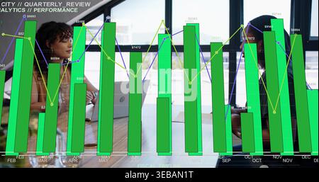 Reviewing two women in sleeveless top, dark blazer using laptops in modern office, green overlay Stock Photo