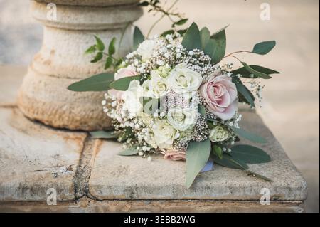 Elegant bridal bouquet with pink and white roses and eucalyptus leaves resting on a stone pedestal. Stock Photo