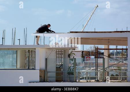 Mallorca Spain - April 25, 2026: A skilled construction worker performs maintenance on a modern white rooftop at the Port de Pollenca marina under a c Stock Photo
