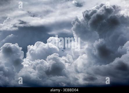 Towering cumulonimbus clouds billow in a dark, moody sky, their dense layers and dramatic forms signaling an approaching storm and shifting weather. Stock Photo