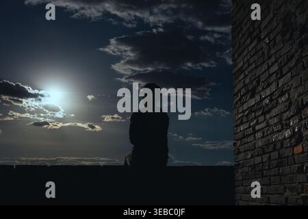 Black backlit young guy silhouette sitting on cliff edge and starry night sky cosmos background. Purpose and success concept Stock Photo