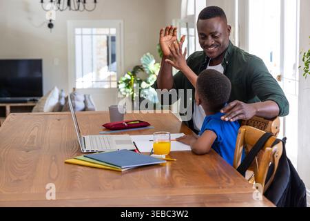 African American father helping son with homework at home table with laptop and pencil, copy space Stock Photo