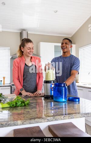 Diverse couple in sportswear preparing pale green smoothie at granite kitchen island with blender Stock Photo