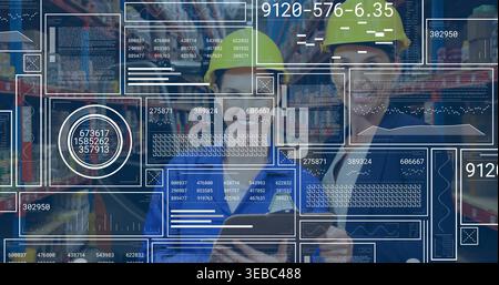 Checking two women in blue coveralls, yellow hard hats using tablet in plant aisle, data overlays Stock Photo