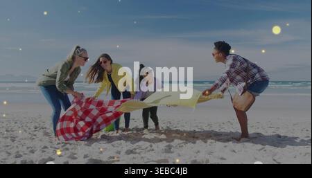 Holding red-white-checkered blanket and yellow sheet, four women crouching on beach with sunglasses Stock Photo