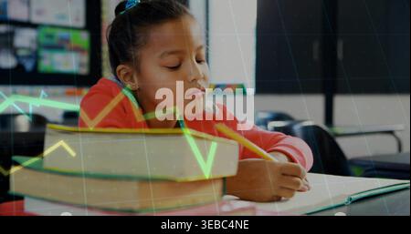 Writing schoolgirl in red sweatshirt using yellow pencil in classroom with notebook and textbooks Stock Photo