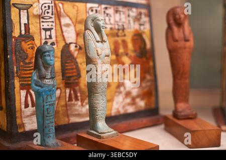 Ancient Egyptian shabti figurines (ushabtis) displayed on wooden stands in a museum setting, featuring turquoise and blue glazed ceramic mummiform Stock Photo