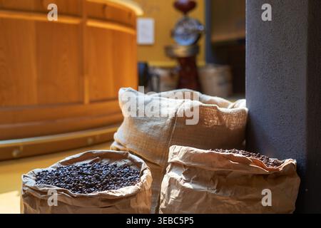 Close-up of dark roasted coffee beans contained in open burlap and brown paper sacks resting on a wooden floor beside a structural column. The Stock Photo