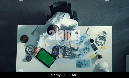 Top down view of skilled engineer writing and planning turbine engine design while sitting at meeting table with gear and electronic generator scatter Stock Photo