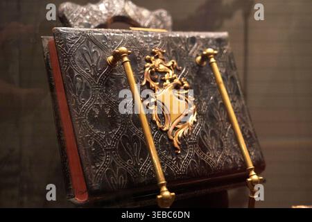 Close-up view of an antique leather-bound book displayed on a stand, likely in a museum setting. The book features an ornate dark brown or black Stock Photo