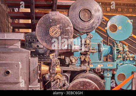 Close-up view of vintage film projection equipment displayed in a museum setting. Multiple antique cinema projectors with large metal film reels are Stock Photo