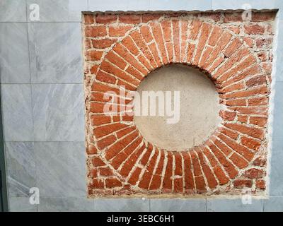 A close-up architectural detail showing a square section of exposed red brickwork set into a wall of grey marble tiles. The bricks are arranged in a Stock Photo