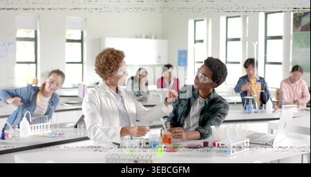 Explaining demo, teacher in lab coat and goggles guiding male student at lab, with test tube Stock Photo