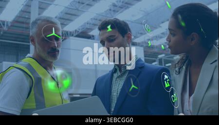 Reviewing laptop in depot, team with hi-vis vest and light blazer viewing green AR icons Stock Photo