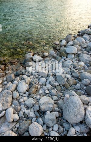 Vertical shot of round pebbles and rocks on the shore of a clear lake or river. Natural texture and geology. Stock Photo