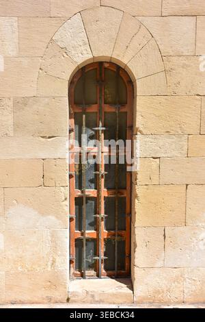 Close view of a narrow arched window with iron bars set in a historic stone wall in Giovinazzo Apulia Italy under bright sunlight Stock Photo
