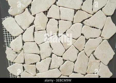 Close-up of small irregular white stone tiles arranged on mesh. Clean and bright natural texture suitable for minimalist interiors and modern design Stock Photo
