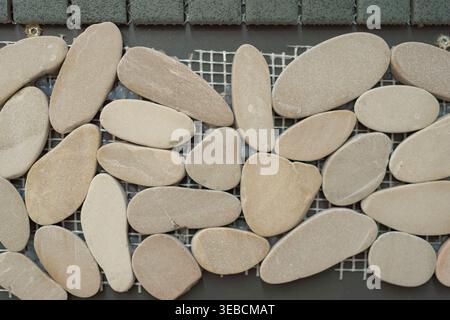Close-up of smooth oval pebble tiles arranged on mesh. Soft natural tones and rounded shapes create a calm organic texture for bathroom, spa, or Stock Photo