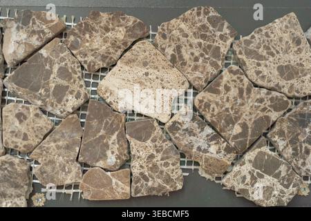 Close-up of irregular brown stone mosaic tiles arranged on mesh backing. Natural texture with organic shapes and earthy tones, ideal for flooring Stock Photo