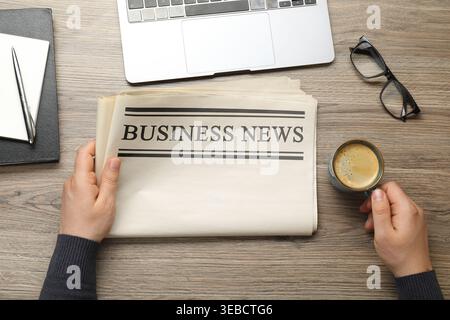 Woman with newspaper and cup of coffee at wooden table, top view Stock Photo