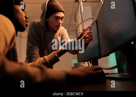 Internet criminals discussing computer system hacking, cyberattack. Hackers in hoodies coding password cracking pogram, scammers programming malicious software at night time Stock Photo