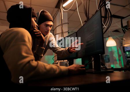 Hackers discussing computer system hacking, coding malicious software, cybercrime. Criminals planning cyberattack, programming internet virus, stealing data at night time Stock Photo