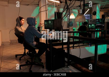 Cybercrime, internet thieves hacking computer system, stealing finances, coding malicious software. Hackers in hoods cracking password, programming internet virus at night time Stock Photo