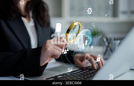 Business Professional Using Magnifying Glass on Laptop with Cloud Technology Icons and Digital Connectivity Elements in Modern Office Environment Stock Photo