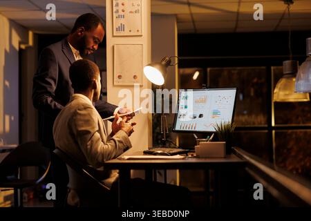 Corporate employees analyzing financial graphs report discussing company strategy in startup office. Executive managers working overhours at investment plan to increase business profit Stock Photo
