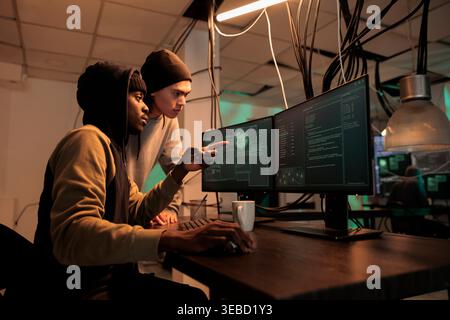 Diverse hackers planning data breach with virus, analyzing firewall encryption to hack computer system. Young team of spies working on breaking database server, steal passwords. Stock Photo