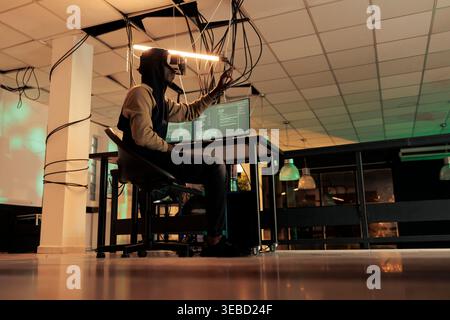 Hacker breaking into computer system in vr glasses, hacking database, spyware coding simulation. African american man cracking server password, data breach in metaverse, cybercrime Stock Photo