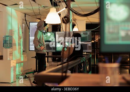 Hackers discussing spyware code, cracking online server password, getting illegal access. Cybertcrime, internet thieves hacking government computer system, developing malware script Stock Photo