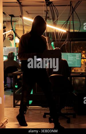 Cyber criminals team hacking computer system, coding malicious software, cracking database password, stealing information, data breach. Cyberterrorism, internet thieves in hoods hacking server Stock Photo