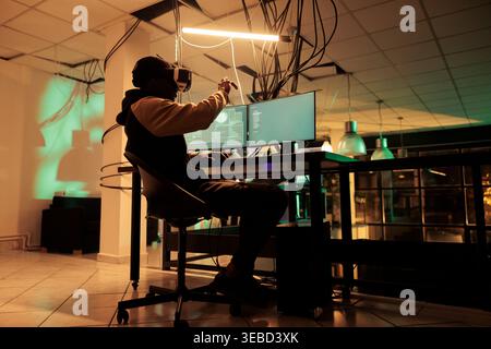 Online criminal using multi monitors and vr glasses to crack encryption and steal passwords. Man trying to hack computer network and system, working with virtual reality headset. Stock Photo