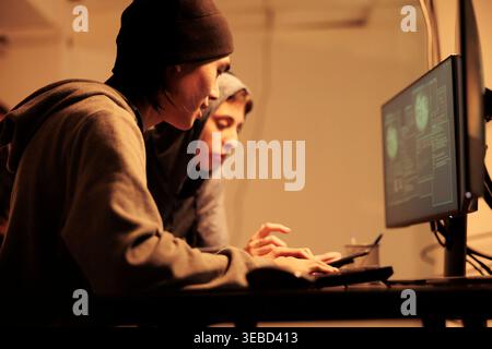 Diverse team of hackers cracking passwords code on screen, working on identity theft and cyberterrorism at night. People planning cyberattack to steal sensitive government information. Stock Photo
