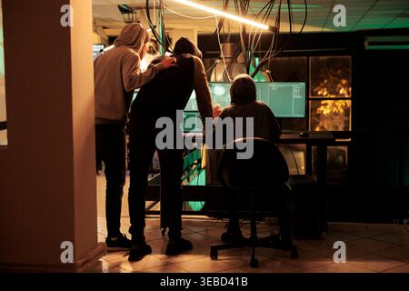 Cyber criminals team hacking database, stealing personal information, hackers running malicious software code. Cyberterrorism, internet thieves in hoodies breaking into server Stock Photo