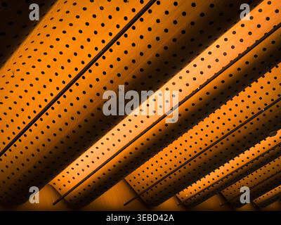 Warm amber light illuminates perforated ceiling panels. Diagonal lines guide eye movement across the image. Uniform holes create rhythmic, repeating p Stock Photo