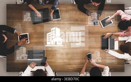 A dynamic business meeting scene featuring diverse professionals engaged in discussions around property data, laptops, and tablets in a modern office Stock Photo