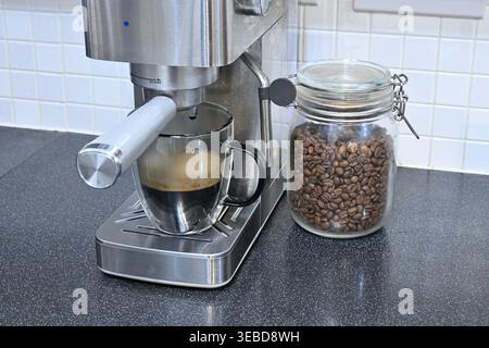 Fresh espresso pouring from machine beside jar of coffee beans Stock Photo
