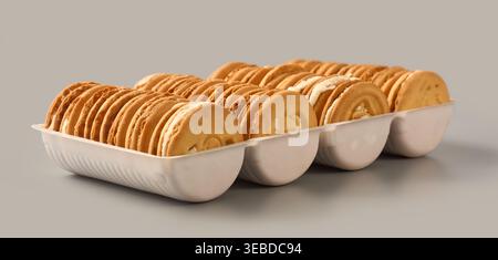 cream sandwich biscuits in white plastic tray isolated grey background, round cookies with textured surface, side view of confectionery retail concept Stock Photo
