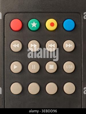 media playback and function buttons on matte black plastic remote control, red green yellow blue and grey rubber buttons with white symbols, top view Stock Photo